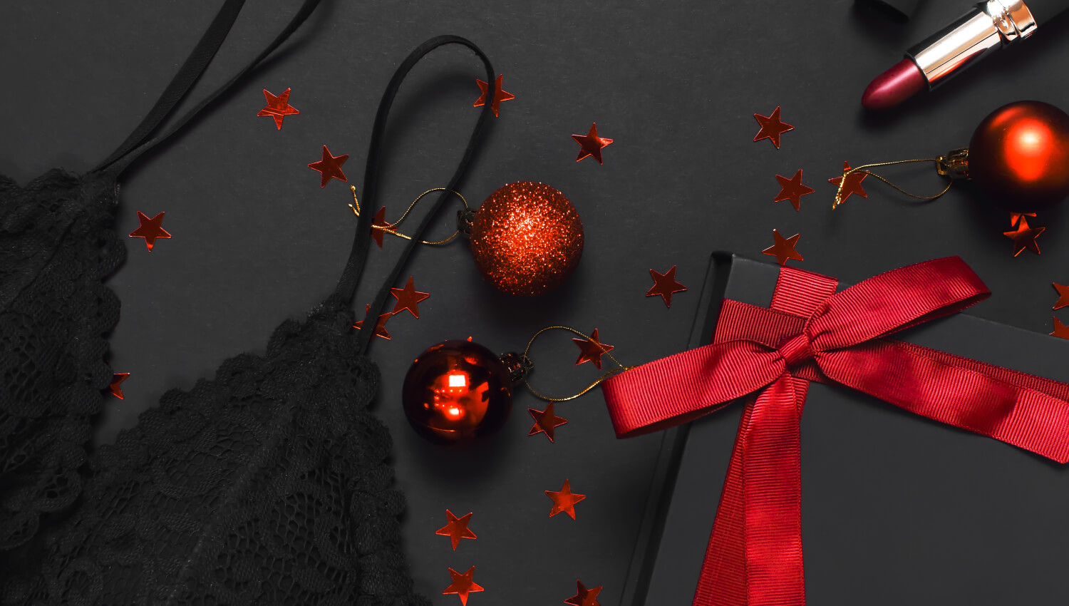 black-gift-box-with-red-ribbon-lace-bra-underwear-red-lipstick-Christmas-balls-holographic-confetti-on-dark-background-top-view-flat-lay-female-essential-accessories